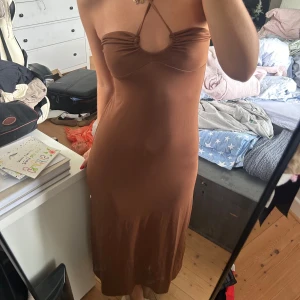 Brun långklänning från GinaTricot  - Säljer denna fina bruna långklänning, som för mig som är 165 cm lång, går ned till strax ovanför anklarna. Den är gjord i ett luftigt tyg och passar perfekt till sommaren. Knyts runt halsen. Använd ett par gånger och i mycket gott skick.