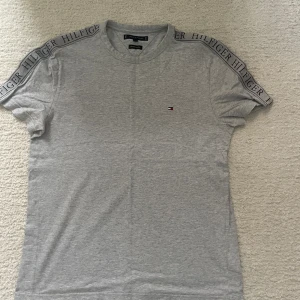 Tommy Hilfiger T-shirt  - Säljer en Tommy Hilfiger  T-shirt  Använd ett fåtal gånger väldigt bra skick storlek Large  Ljusgrå  