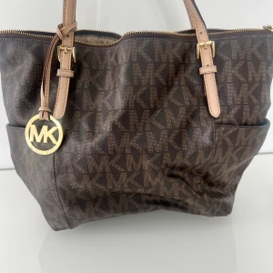 Michael kors väska - Säljer denna bruna Michael kors väskan med guldiga detaljer. Säljes då den inte längre kommer till användning. Väskan är lite sliten fler bilder kan fås.  Nypris 4000 kr  Mitt pris 1800 kr  