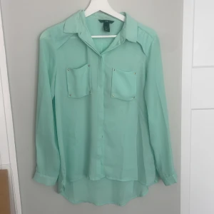Mintgrön skjorta h&m - H&M skjorta  Storlek 34  100% polyester Fin mintgrön färg med guldiga detaljer, lite mesh-känsla på tyget → lite snyggt genomskinlig  Har två knappt synliga fläckar, dessa går med all säkerhet bort i tvätt 