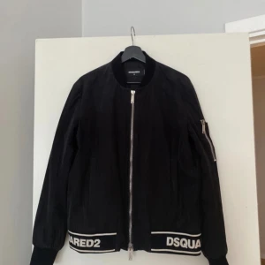 Dsquared2 bomberjacka  - Svart bomberjacka med vita detaljer. Jackan har två fickor på framsidan och en ficka på vänster ärm. Den har en dragkedja framtill och ribbstickade muddar och nederkant.