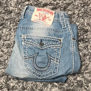 FETA BAGGY TRUE RELIGION JEANS - Ett par baggy ljusblåa True Religion Jeans. Skicket ca 7.5/10, finns limrester på insidan av byxorna (inte synligt) och styngnen på taggen där bak har gått upp en aning. Säljer för att de är för små, välkomnar prisförslag.