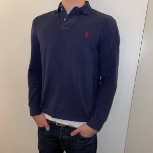 Tröja Polo Long Sleeve Piké - Fin marinblå tröja från Ralph Lauren. Tröjan har ett litet hål vid höger axel, dock är det knappt märkbart, men jag väljer ändå att sälja tröjan billigare pga detta.