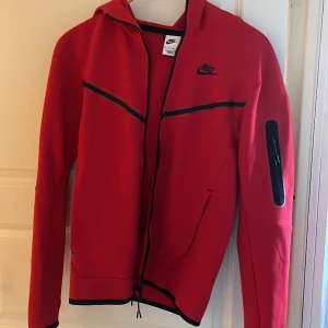 Röd Nike tech fleece Hoodie - Hoodien var köpt för en månad sedan. Köpt på Niketown i London. Använts Max 5 gånger. Har inga fel eller problem. Köpt för 1200 kr