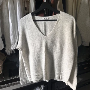 Stickad tröja  - Beige/krämvit stickad tröja med en V-ringning framtill