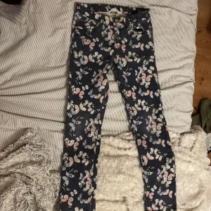 Blommiga byxor från H&M - Ett par byxor från H&M med fjärilar på i storlek EUR 134 (8-9 år). Byxorna har ett mönster av fjärilar i rosa och vita nyanser på en mörkblå bakgrund. De har en knapp med texten 'Enjoy the little things in life' och de är stretch 