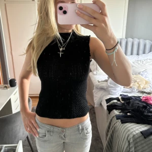 Svart ribbad ärmlös topp - En svart ribbad ärmlös topp i storlek S. Toppen har en tight passform och är tillverkad i ett stretchigt material som framhäver figuren. Perfekt för både vardag och fest.