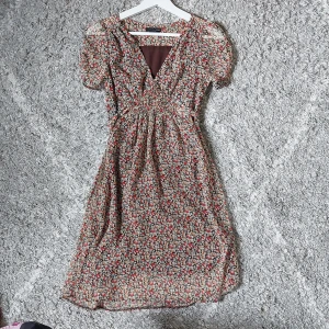 Blommig klänning från H&M - En blommig klänning från H&M i storlek XS. Klänningen har korta ärmar och en v-ringad hals. Justerbar storlke tackvare ett elastiskt midjeband och knytband i ryggen. Använd ca 1 gång och säljer då den är för liten för mig.