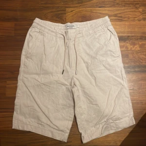 Beige shorts från Dressmann - Säljer ett par bekväma beige shorts från Dressmann i storlek S. De är gjorda av en linneblandning och har en elastisk midja med dragsko för justerbar passform. Shortsen har två sidofickor och två bakfickor med knappar. Perfekta för varma sommardagar!