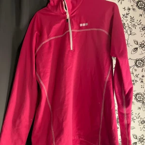 Rosa långärmad tröja med dragkedja - Säljer en snygg rosa långärmad tröja med dragkedja framtill. Perfekt för kyliga dagar eller som ett extra lager under jackan. Tröjan har vita sömmar som ger en fin kontrast och en sportig look. Passar både till vardags och träning.