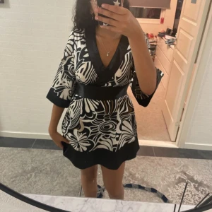 Klänning  - En super söt klänning med vita, svarta och bruna mönster som man knyter där bak 