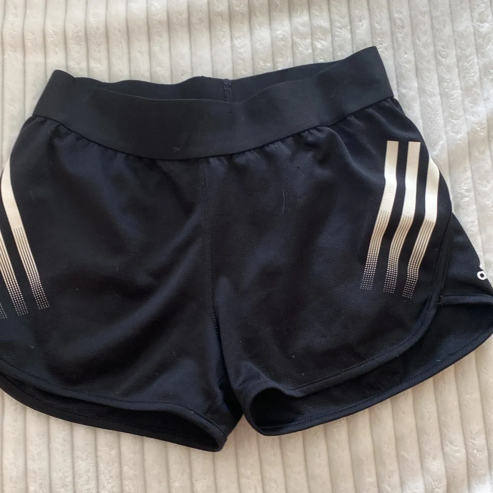 Ett par svarta shorts/hot pants från Adidas med vita ränder på sidorna. Shortsen har en bred elastisk midja och är tillverkade av ett lätt och andningsbart material. säljer pga att dom är lite försmå 🌟. Shorts.