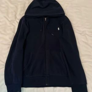Ralph lauren zip hoodie - Ralph Lauren zip hoodie som är mörkblå och i storlek L den är använd men i bra skick bortsätt från att taggen i nacken är bort tvättad