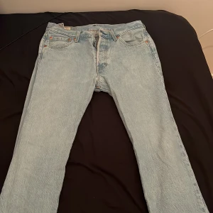 Ljusblå jeansbyxor från Levis - Ett par ljusblå jeansbyxor från Levis. Byxorna har en klassisk femficksdesign och en dragkedja med knappstängning. De har en rak passform och är tillverkade i denim.