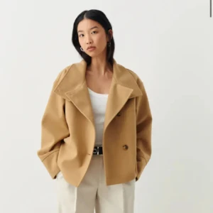 Beige kappa med knappar - Säljer en snygg beige kappa i storlek S. Den har en modern och stilren design med stora knappar framtill och en hög krage som kan vikas ner. Jackan är långärmad och har en lös passform som gör den bekväm att bära. Perfekt för höst och vår!