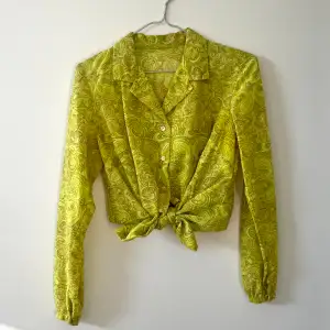 Skjorta/blus från 70-talet med underbart paisley-mönster. Lite genomskinlig, somrig och lysande grön. Jättefin uppknuten i midjan. 