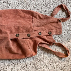 Superfin beige, rosa hängselbyxa - Supersnygg hängselbyxa i beige, rosa färg. Jag älskade dessa byxor, tyvärr är dem för små nu. Passar perfekt med en t-shirt. Ascoola!!