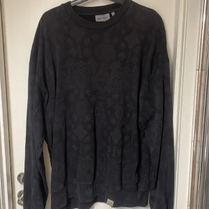 Carhartt sweatshirt - Snygg svart sweatshirt från carhartt med mönster på, mönstrerna syns inte så mycket. Använder aldirg längre, därför jag säljer.  Strl L, sitter lite baggy. Skick 9/10  Nypris runt 1000kr 