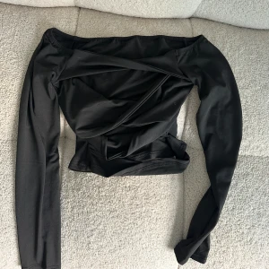 Svart långärmad topp - En svart långärmad topp med en unik omlott-design framtill. som ny och perfekt till fest 