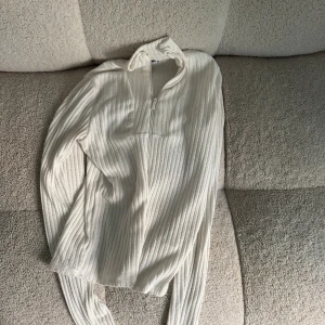 Vit ribbad tröja med dragkedja - En vit ribbad tröja med dragkedja framtill. Tröjan har långa ärmar och en hög krage.