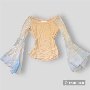 Vintage Beige off-shoulder topp - En jättecool beige off shoulder tröja. Detaljrika utsvängda ärmar som är ljusblå med beiget mönster på. Tunt och skönt material.  Ganska sliten i ärmhålorna. 