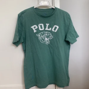 Grön Ralph Lauren t-shirt - Tja! Säljer denna gröna Ralph Lauren t-short i storlek 14-16 år/Xs-S. Den har en fläck som ni ser på sida 3 som är svår att få bort men går säker med rätt medel annars är tröjan i väldigt bra skick. Säljer den för 129 Kr. Priset kan diskuteras.