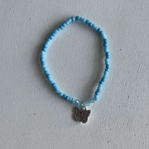 Egengjorda armband - Ett egengjort pärlarmband med färgeren blå i olika nyanser med en blandning pärlsorter. Armbandet har en berlock i silver som avbildar en fjäril. 