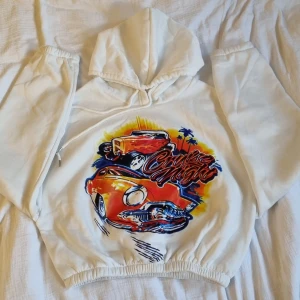 Magtröjehoodie med tryck  - Vit magtröjehoodie med snyggt bil tryck, skönt material, lite varmt så passar perfekt mot hösten och tidig vår, resår vid magen som ändrar efter just din kroppsform 