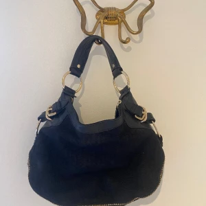 DKNY axelväska - Liten och tuff DKNY väska i skinn och tyg med klassiska loggor på tyget. Gedigen med snygga detaljer i guld. Har bara blivit hängande de senaste åren. Inköpt från Jackie för många år sedan. Ungdomlig modell men passar alla åldrar.  Ca 32 x 24 cm. 