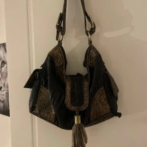 Vintage väska  - Säljer denna svarta väska med guld detaljer! Den är sliten på baksidan (bild 3) men det är inget som syns när du använder väskan! Har även ett litet hål inuti!