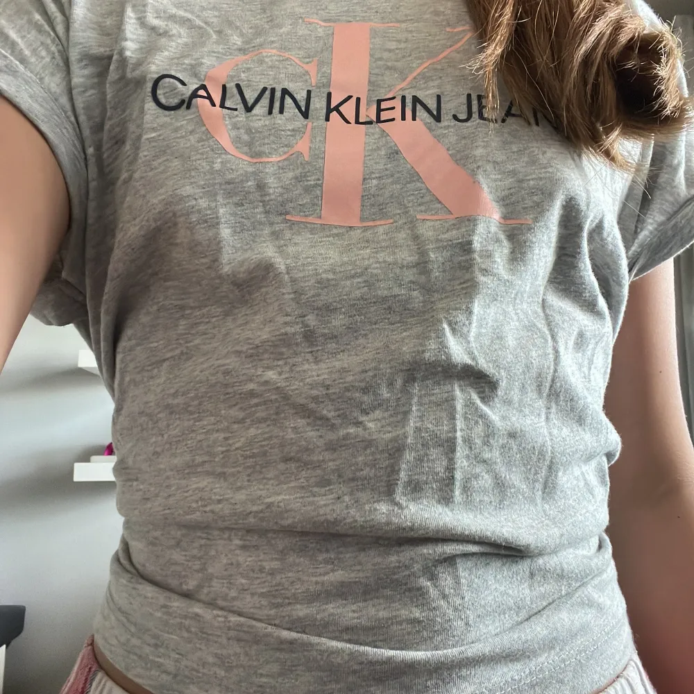 Säljer denna gråa Calvin Klein t-shirten med rosa text för jag inte använder den. (ÄKTA) 💕 Storlek 12, lite skrynklig men försvinner efter användning. Priset kan diskuteras 💕 100kr. . T-shirts.