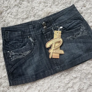 Jeanskjol  - Helt ny svart/blå lågmidjad jeanskjol från R.marks, så unik med coola detaljer. Storlek 25. Total längd:25cm midjemått:36 (x2) + lite stretch. Vill du köpa trycker du på köp nu, jag postar inom 24h