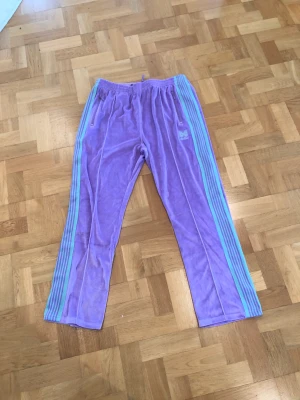 Needles x awge velour track pants - Storlek: M Condition: 9/10, lappen är borttagen men byxorna har bara testats ett par gånger Färg: Lila/rosa+mintgröna ränder  Frakt betalas av köpare om vi inte kommer överens om något annat