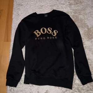 Säljer Hugo Boss tröja som är svart med guld text. Tröjan är knappt använd och i god skick. Storleken är S/M, men skulle säga att tröjan passar mer den som har M. Tröjan är förstås äkta. Skriv för fler frågor eller bilder!