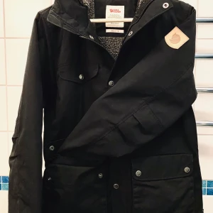 GREENLAND WINTER JACKET W - Slitstark i vind- och vattenavvisande G-1000 Eco. 65% återvunnen polyester, 35% ekologisk bomull. Kan impregneras med Grönlandsvax för extra väderskydd. Teddyfleece-foder i polyester. Ärmtyp: Lång ärm Huva: Ja Egenskaper för huva: Fast huva Stängning: Tryckknappar, Tvåvägs dragkedja Klädlager: Ytterlager Antal fickor: 7 Fickor: Bröstficka(or) med knappar, Handficka(or), Innerficka(or)  Rygglängd storlek s: 69 cm Vikt storlek s: 1100 g