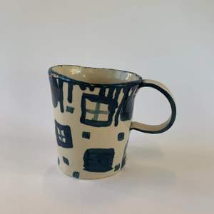 En handgjord kopp i keramik med en naturlig sandfärgade samt ett blått motiv. 