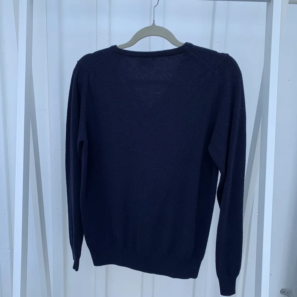 En v-ringad tunnstickad tröja ifrån GANT i en marinblå färg och med ett vitt broderat märke på vänster bröst. Endast använd en gång och är i nyskick. (Material: 80% ull och 20% polyamid). Tröjor & Koftor.