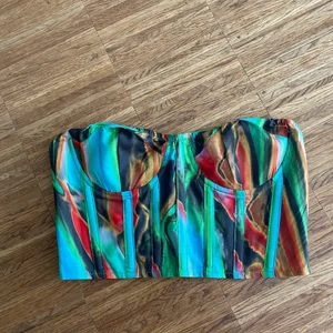 Strapless topp - Cool topp från PLT. Storlek 34. Toppen stängs med dragkedja i ryggen. Färgerna går i grön, blå, och detaljer av rött, gult, svart.