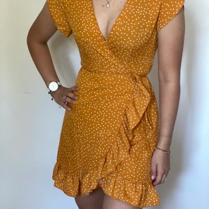 Gulprickig klänning - Gul, v-ringad, kort omlottklänning med fina volanger längs sidan. Aldrig använd. 