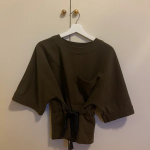 Tshirt med knytning strl. S - En mörkgrön tshirt i sweatshirt material med knytning i midjan och ficka på vänster sida. Köpt från Zara och är i storlek S. Använd några gånger men är i bra skick. Säljer för 150kr + frakt.