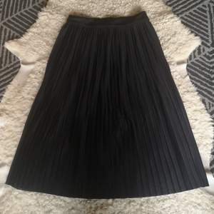 En fin plisserad svart kjol med dragkedja och och knapp på sidan. Fint fall och snygg passform. Fint skick! . 