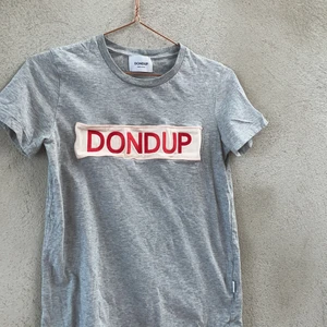 Grå Dondup T-shirt  - En grå DONDUP med tryck på magen. Helt oanvänd, pga fel storlek. Tröjan har  ett litet märke på baksidan vid nacken. 