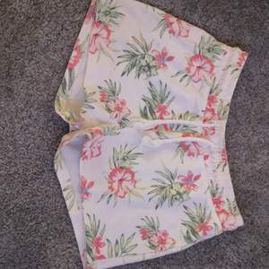 Vita mjukis shorts med rosa exotiska blommor. Är i väldigt fint skick och knappt använda. De har resor i midjan men de går att knyta dem framme. Storlek: 158/164. Inga fickor. 