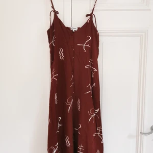 Midiklänning Weekday med knytband - Brun/röd midiklänning med vitt mönster. Knytbara axelband, knytningen kan ändras, ganska långa band. Från Weekday, storlek xs. 