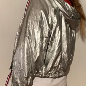 Tommy Hilfiger windbreaker strl m - Windbreaker från Tommy Hilfiger som ser ut som ny, inga slitningar och är sparsamt använd, super cool silverfärg på utsidan med ett rött foder, perfekt för våren, nypris 1200kr, köparen står för frakten
