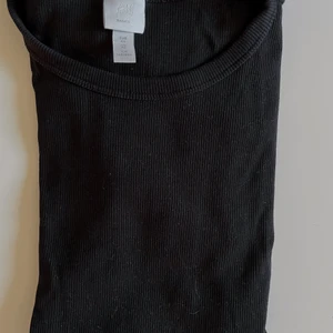 T-Shirt - Svart ribbad, helt vanlig T-shirt från HM. Väldigt användbar! Sitter tight men är stretchig.