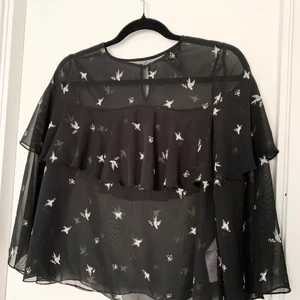 Svart blus med fågel motiv och volanger  - Denna har varit en av mina favorit tröjor. Super fin och härlig. Säljer för att min stil förändrats. Använt en del men är fortfarande jätte fint skick! 