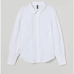 Bomulskjorta med puffärm  - Skjortan har krage och knäppning fram samt lätt intagen midja. Vid, rynkad puffärm med smal smock och manschett vid ärmslut. 