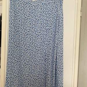 En lång blå kjol med blommigt mönster. Kjolen är aldrig använd och är i storlek 40. På ena sidan finns det en slit.