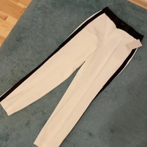 Kostymbyxor - Ett par helt oanvända kostymbyxor med sin prislapp på. Jättefina svarta detaljer i midja och längs benen. Storlek: S